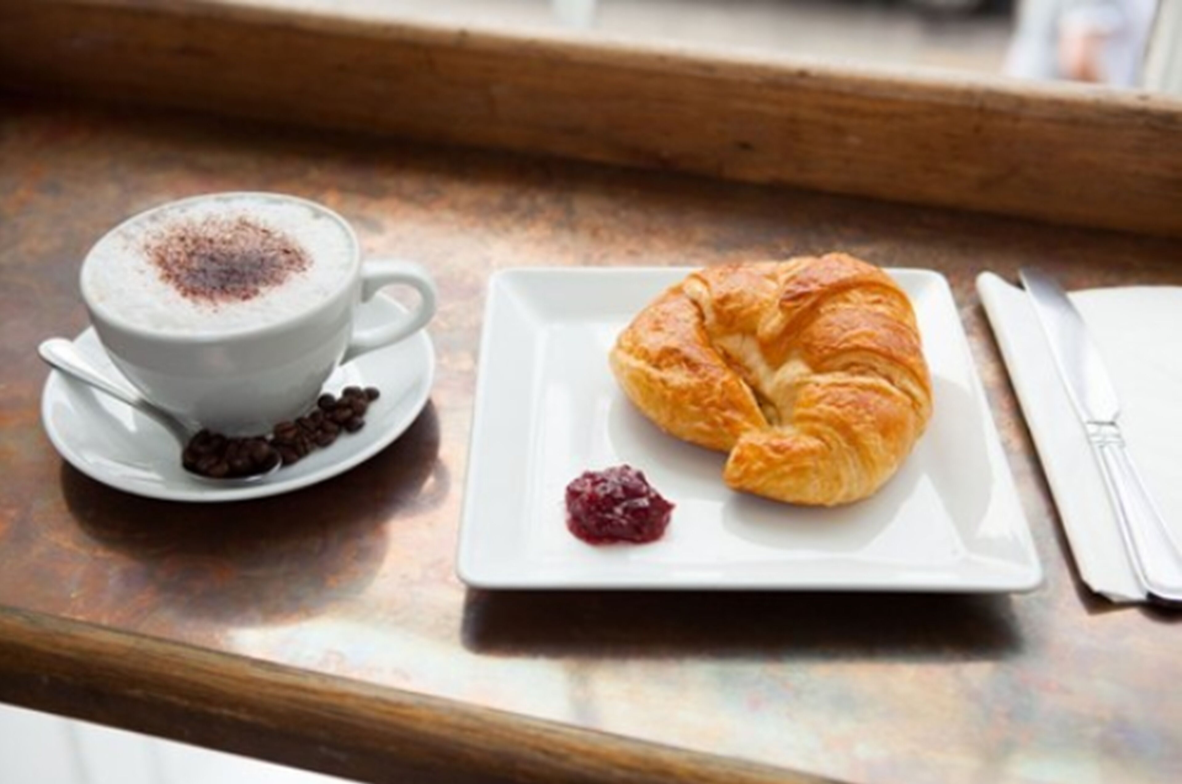 A table with a cup of coffee and a croissant on a plate.