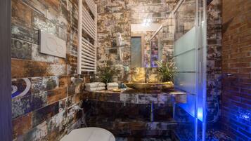 Un baño con pared de azulejos rústicos, un lavamanos moderno y una cabina de ducha de vidrio.