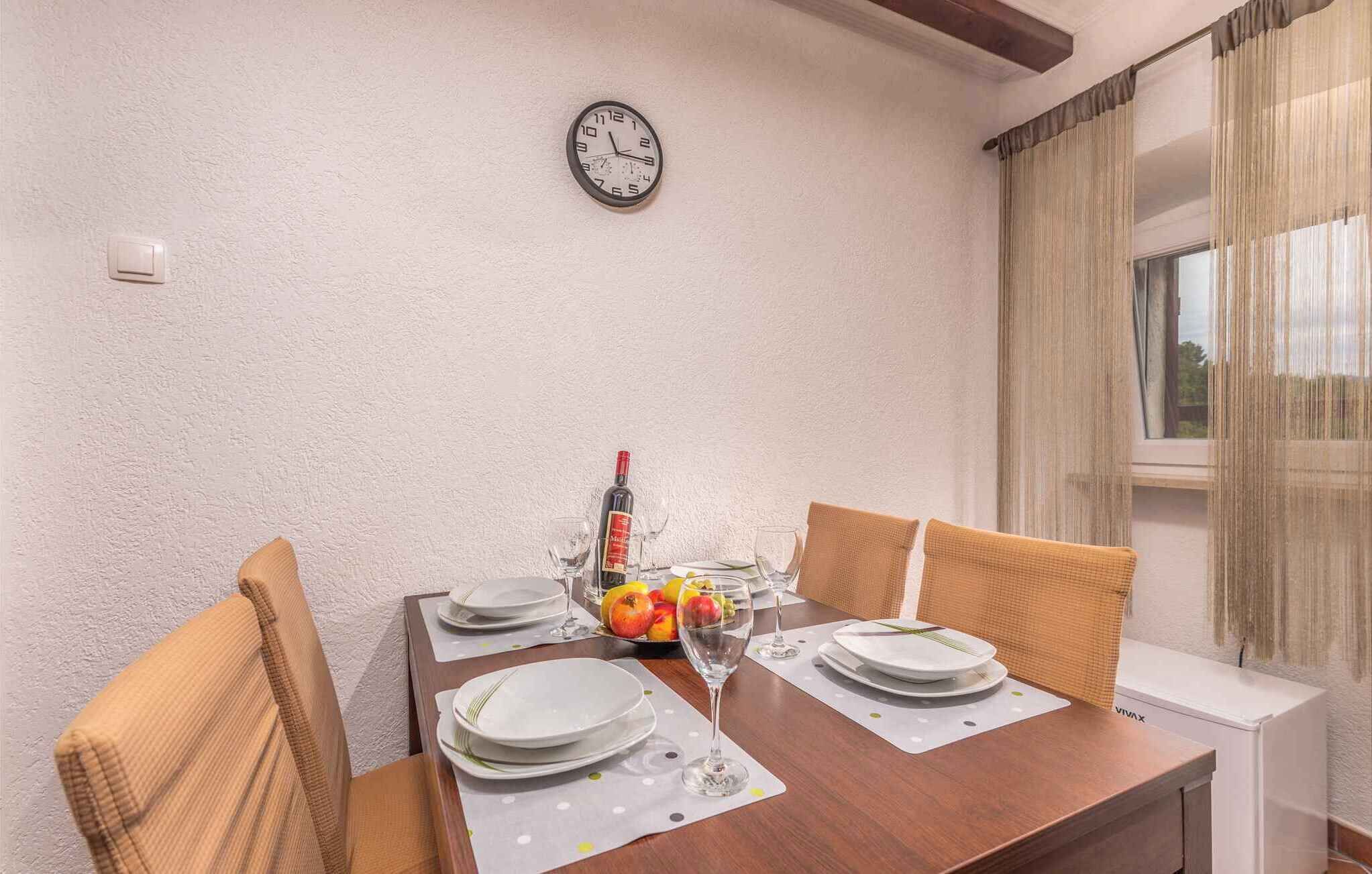 A dining table set with plates, glasses, and a bottle of wine, with a clock on the wall and a window with curtains.