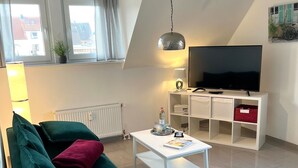 Una sala de estar moderna con un sofá verde, una mesa de centro blanca y un televisor de pantalla plana sobre un mueble blanco.
