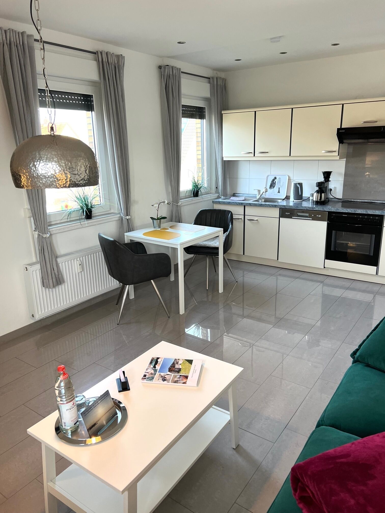 Un salon moderne avec une table basse blanche, un canapé vert et un coin repas comprenant une table blanche et des chaises noires.