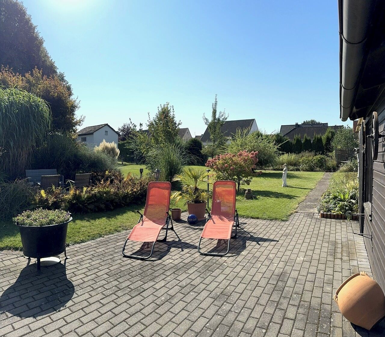A paved patio with two lounge chairs and a potted plant.