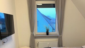 Una habitación de hotel moderna con una cama, un banco, un televisor y una ventana con cortinas.