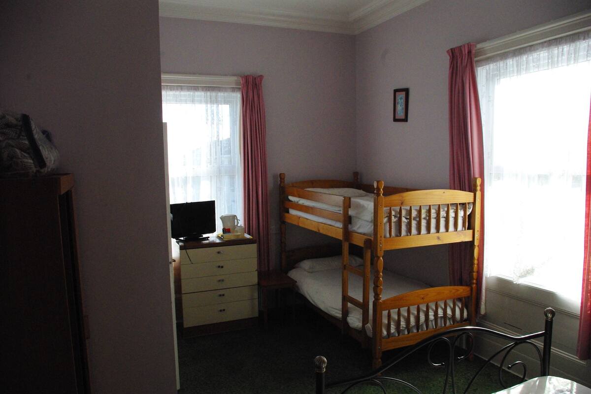 A room with bunk beds, a desk with a computer, and a window with curtains.
