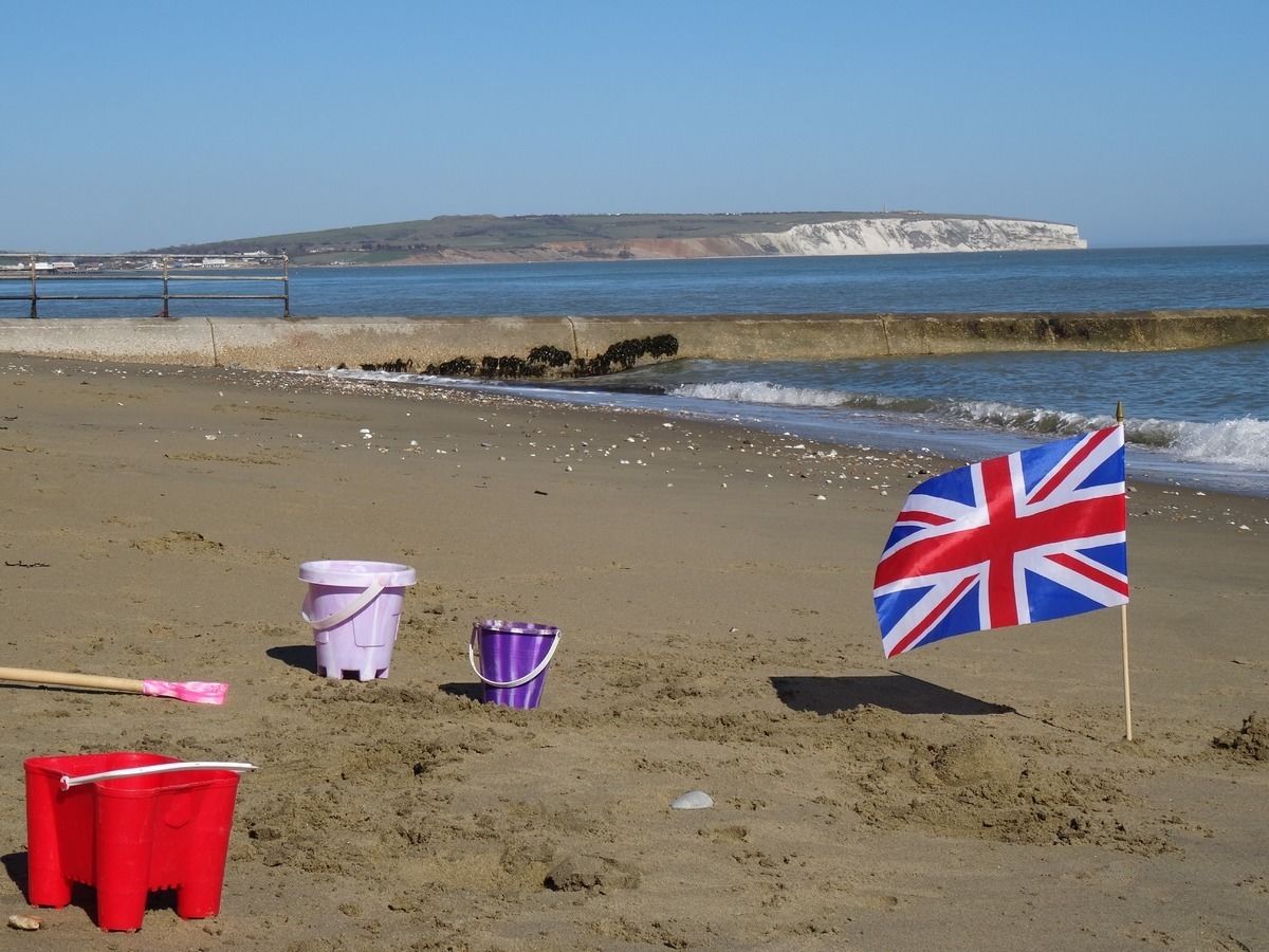A beach with a flag, buckets, and a stick.