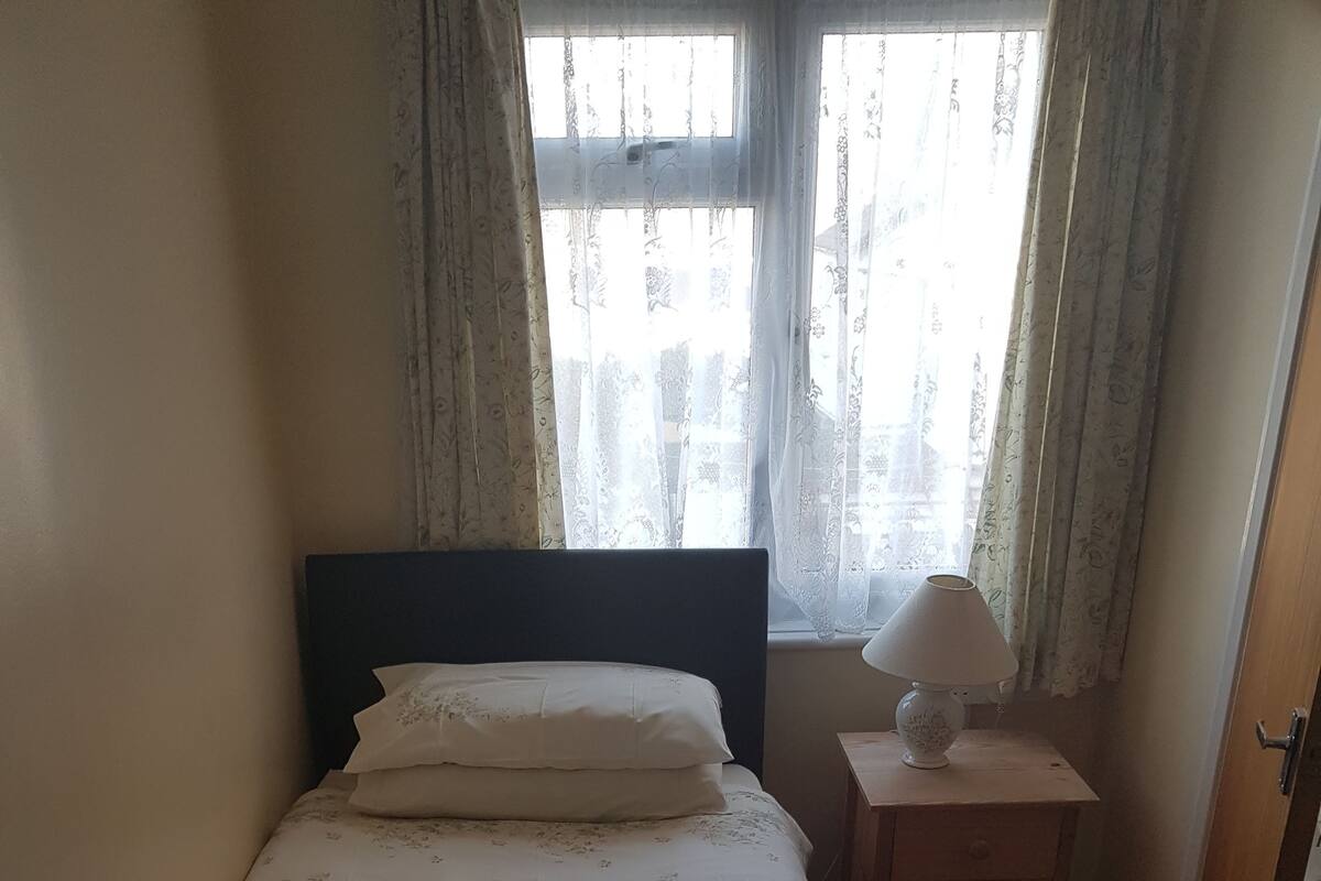 A neatly made bed with floral bedding, a bedside lamp, and a blue book on the bed.