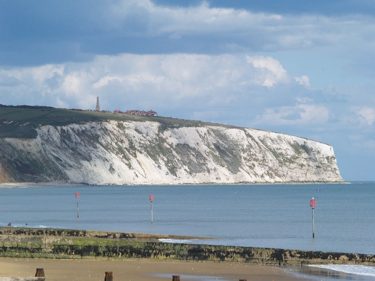A coastal landscape with white cliffs, a beach, and a lighthouse.
