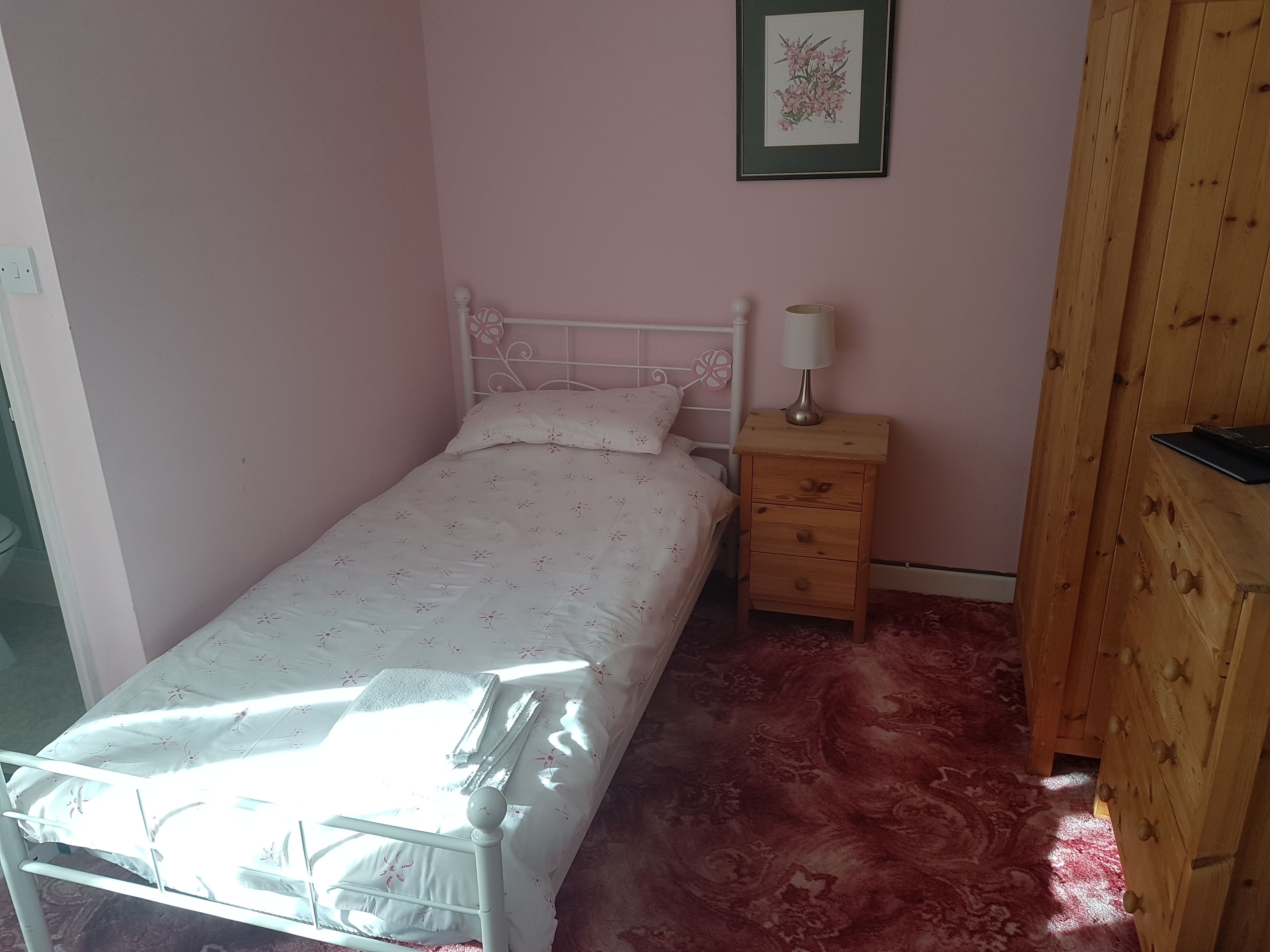 A small bedroom with a single bed, a bedside table with a lamp, and a wooden wardrobe.