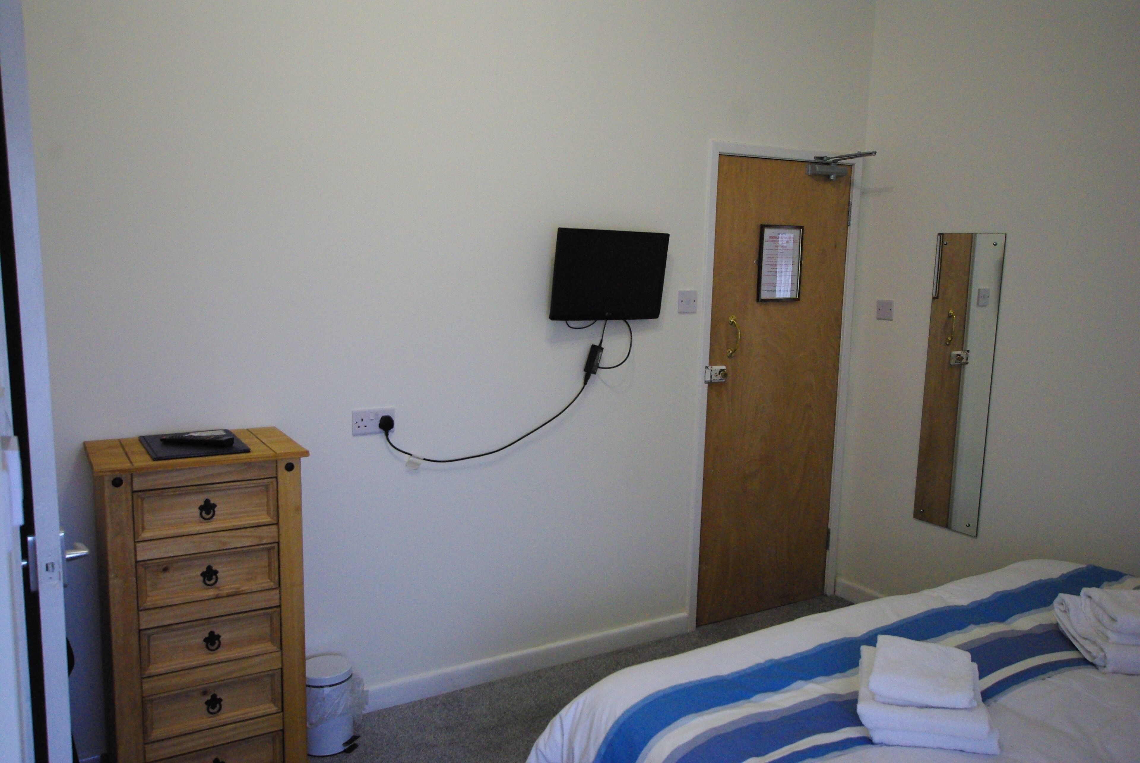 A bedroom with a bed, a wooden dresser, a television mounted on the wall, and a door with a mirror.