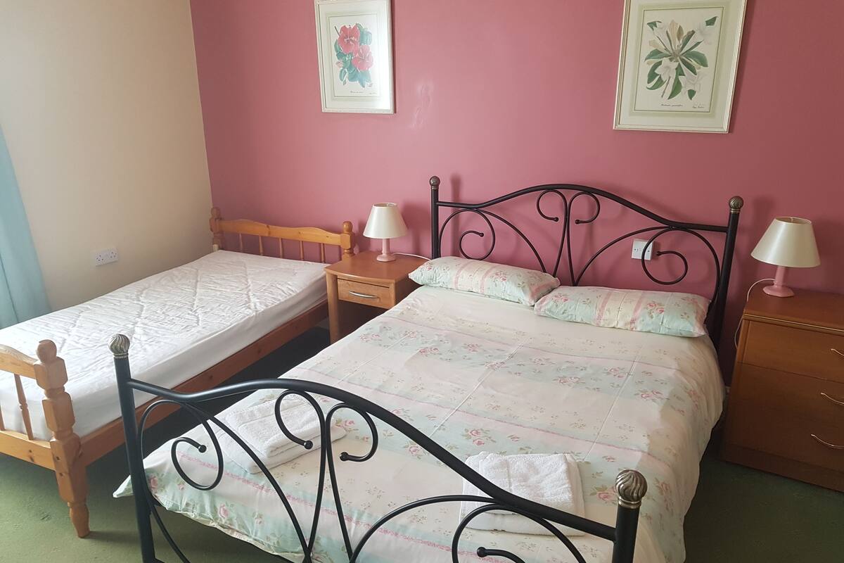 A bedroom with two single beds, a wooden nightstand, a dresser, and two wall-mounted lamps.