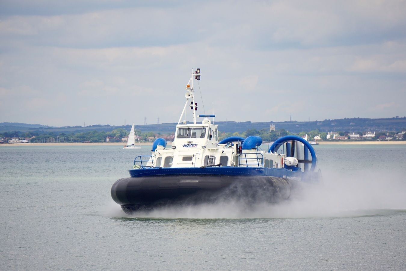 A hovercraft moving across a body of water, with a coastal landscape in the background.