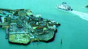 An aerial view of a coastal town with a ferry dock, buildings, and a waterfront promenade. - Sandhill (Sandown)
