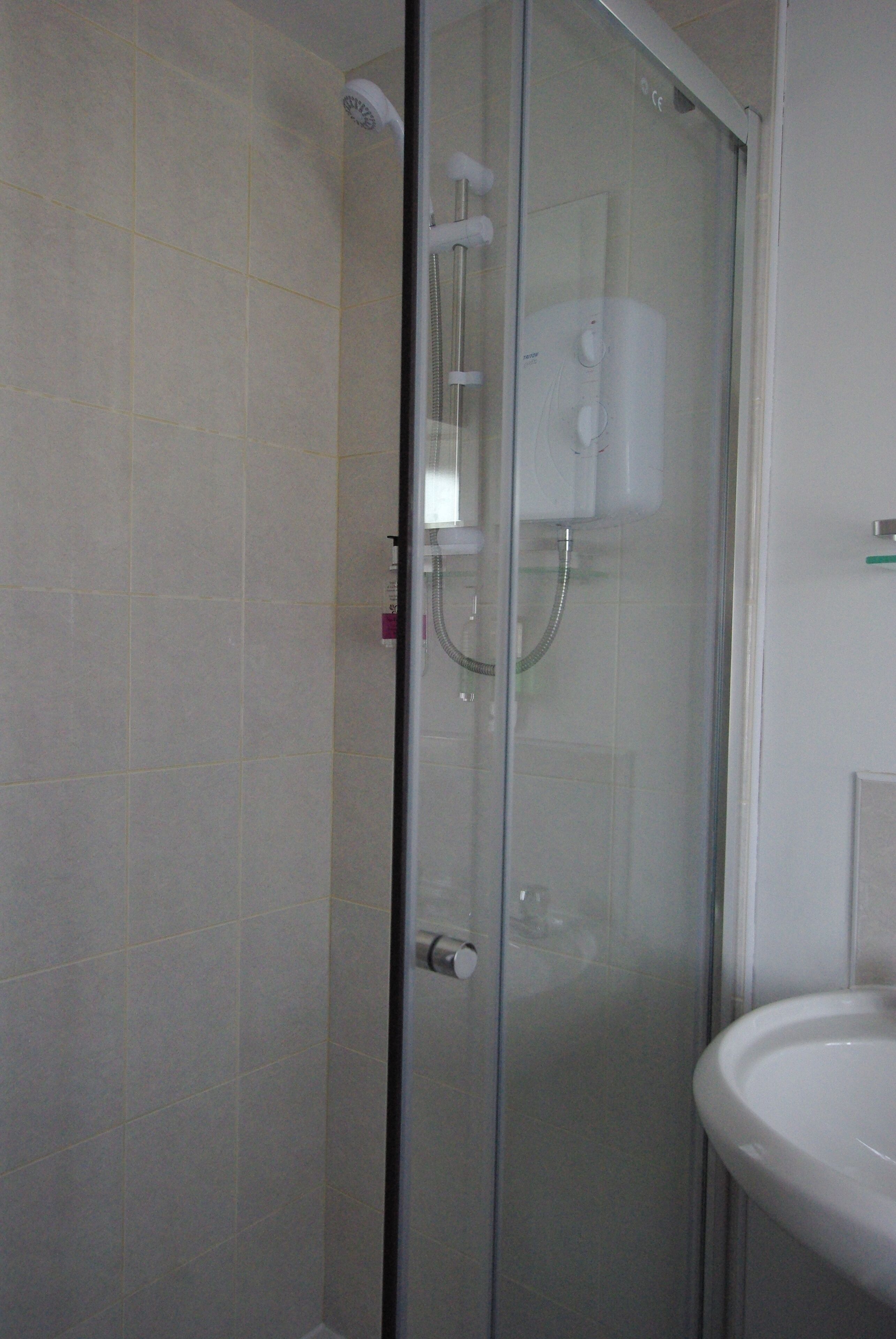 A glass-enclosed shower with a control panel, a white sink, and tiled walls.