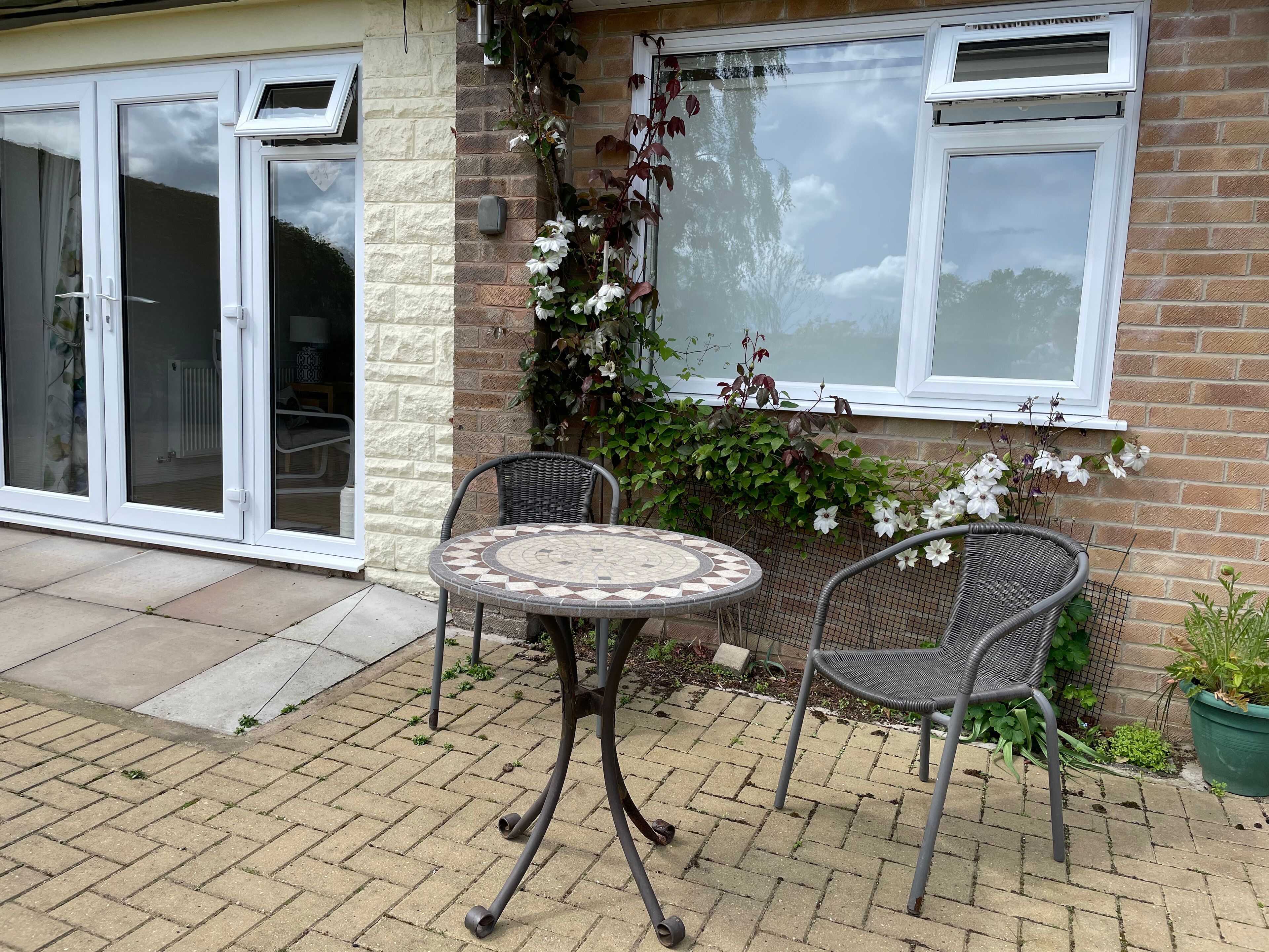 A patio with a round table and two chairs, a brick wall, a window with a view, and a door with glass panels.