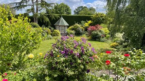 A garden with a gazebo, various flowers, and neatly trimmed hedges.
