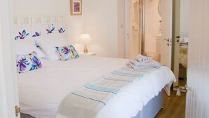 A neatly made bed with floral pillows, a bedside lamp, and a view of a bathroom through an open door.