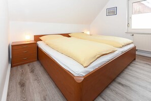 A double bed with a wooden frame and white bedding in a room with a sloped ceiling and a window.