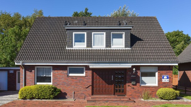 A two-story brick house with a dark tiled roof, a front door with a window above, and a small front yard with two bushes.