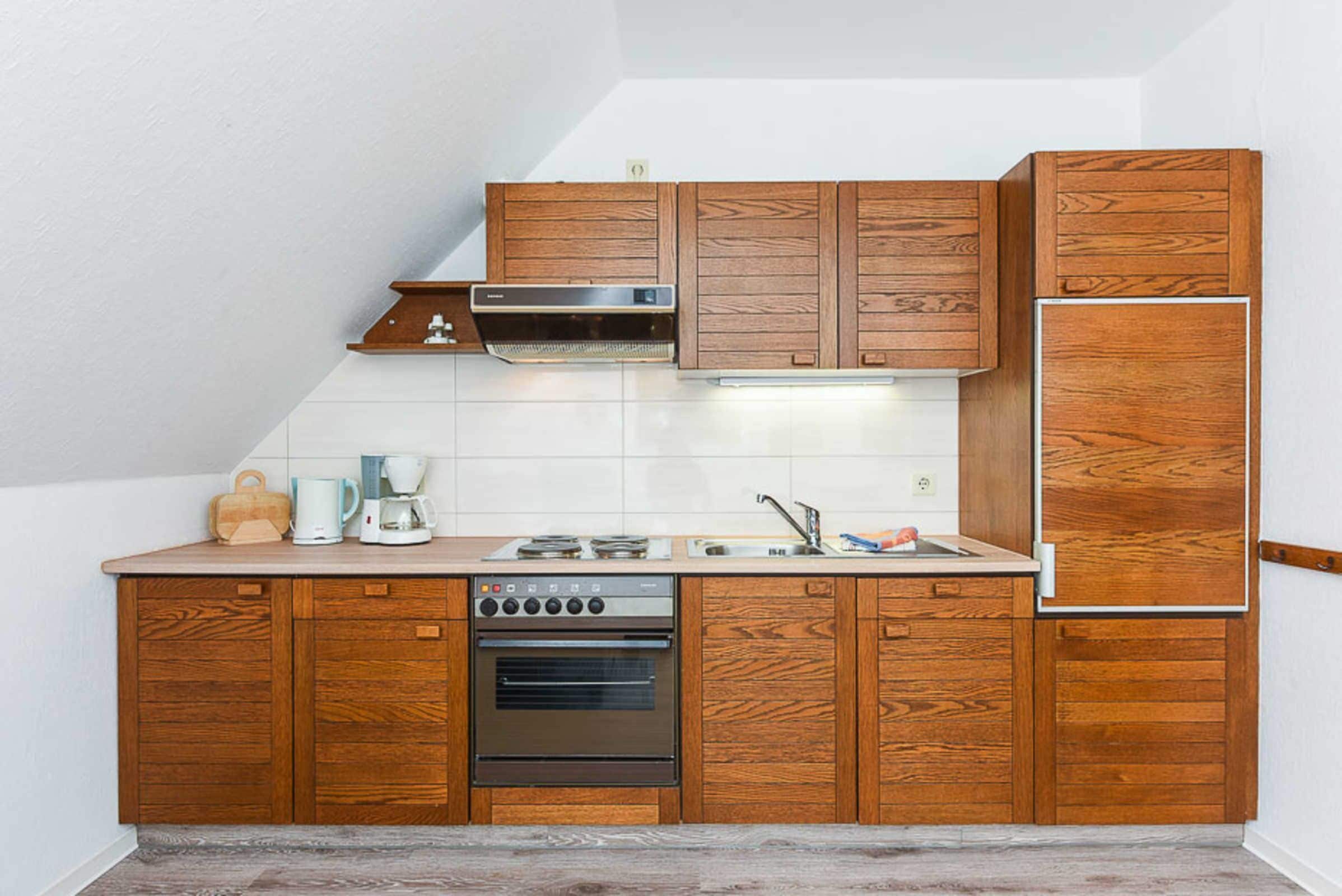 Eine kleine Küche mit Holzschränken, einem Einbauofen, einer Mikrowelle und einem Edelstahl-Kühlschrank.