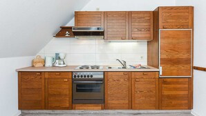 A compact kitchen with wooden cabinets, a built-in oven, a microwave, and a stainless steel refrigerator.