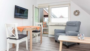 A room with a television mounted on the wall, a grey sofa, a wooden table, and a white chair.