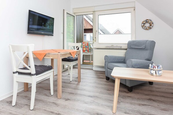 A room with a television mounted on the wall, a grey sofa, a wooden table, and a white chair.