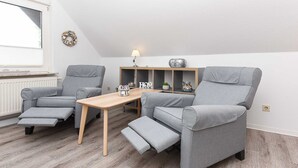 A modern living room with two grey recliner sofas, a wooden coffee table, and a shelf with decorative items.