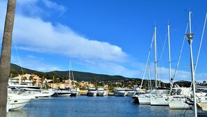 Marina con varios yates amarrados, cielo azul despejado y montañas al fondo.