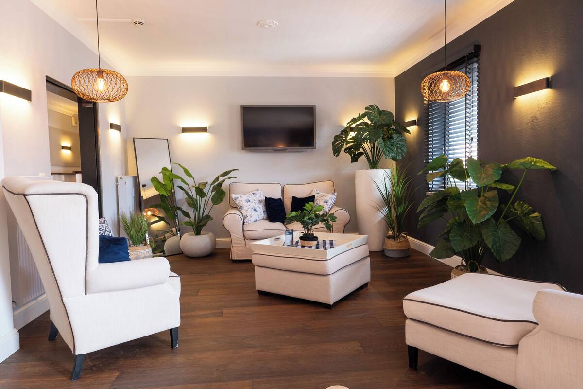 A modern living room with a sofa, armchairs, a coffee table, and large potted plants.