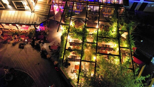 An aerial view of a rooftop garden with seating areas, surrounded by buildings with illuminated windows. - Alpenliebe Design Hotel (Inzell)