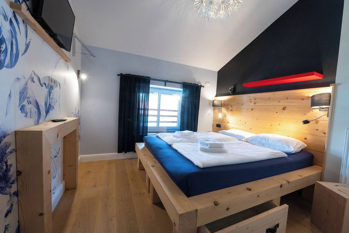 A bedroom with a wooden bed, a desk, and a window with curtains.