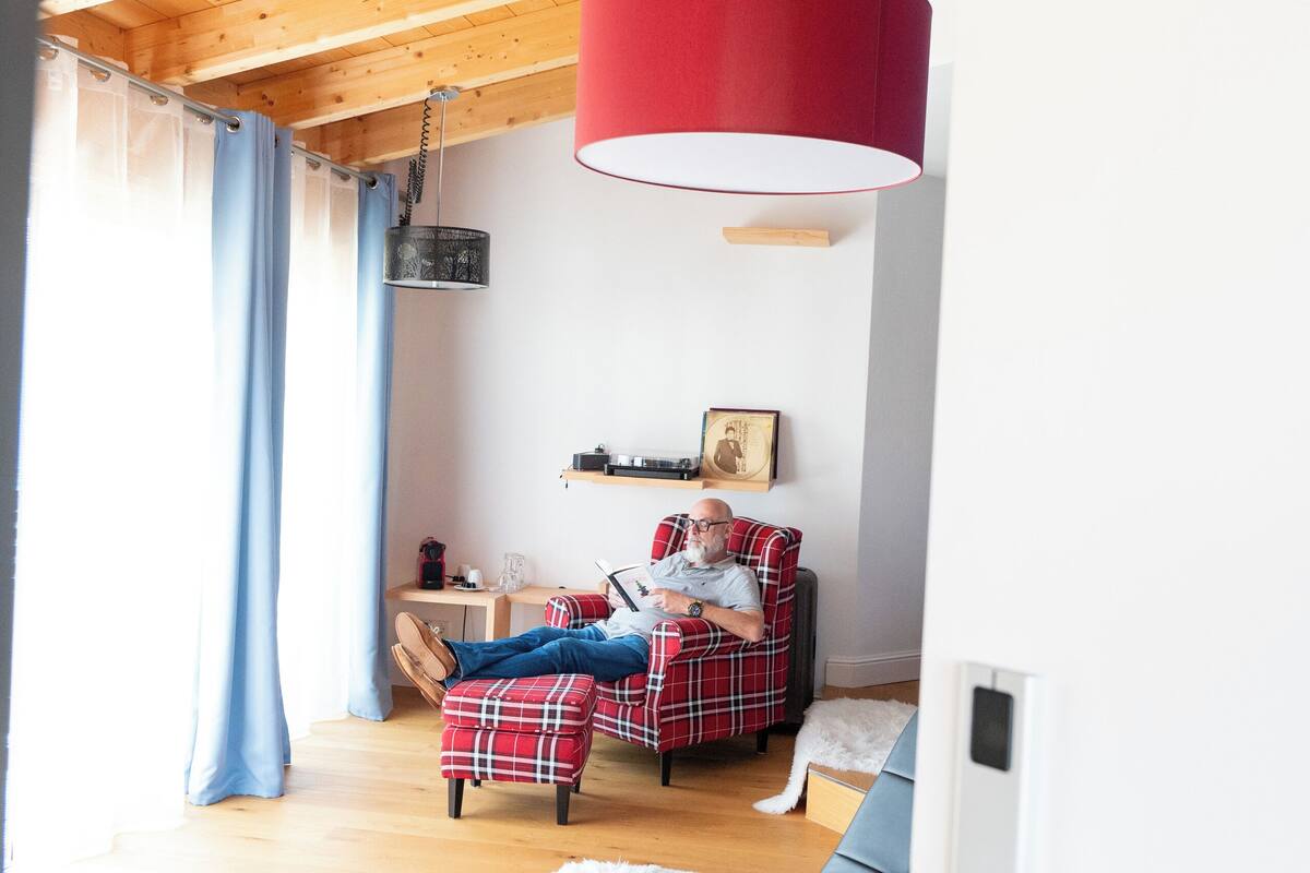 A cozy living room with a wooden ceiling, a red hanging lamp, a plaid sofa, and a white furry throw.