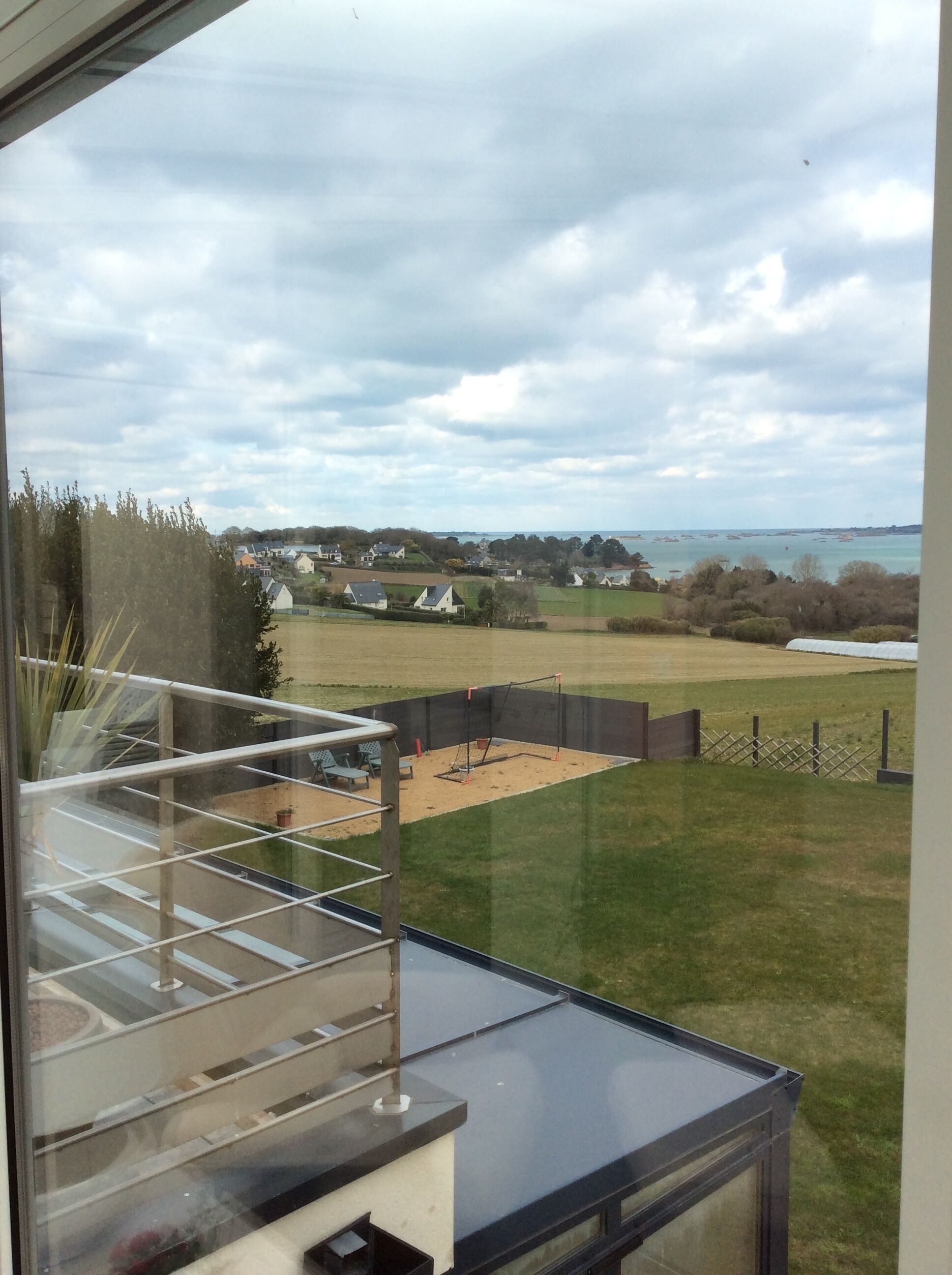 A view from a balcony with a glass railing, overlooking a grassy area with a swing set and a sandy play area.