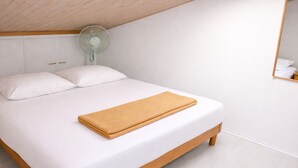 Una cama individual con ropa de cama blanca y un cabecero de madera, una mesita de noche y un ventilador de pared.