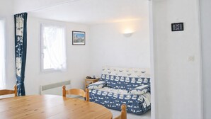 Una habitación con una mesa de madera, un sofá estampado con motivos náuticos, un cuadro en la pared y una ventana con cortinas.