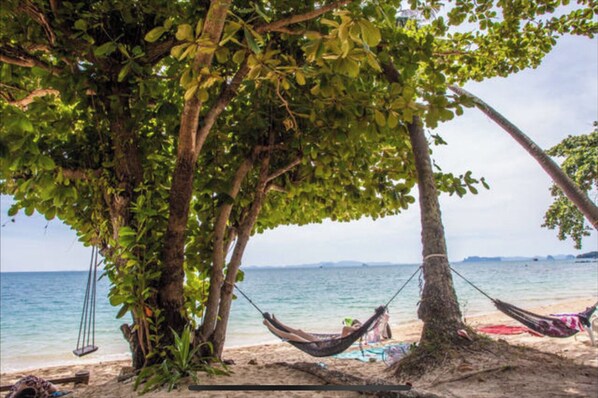 Relax in a shaded hammock, suspended between two trees, overlooking the calm sea and distant landforms.