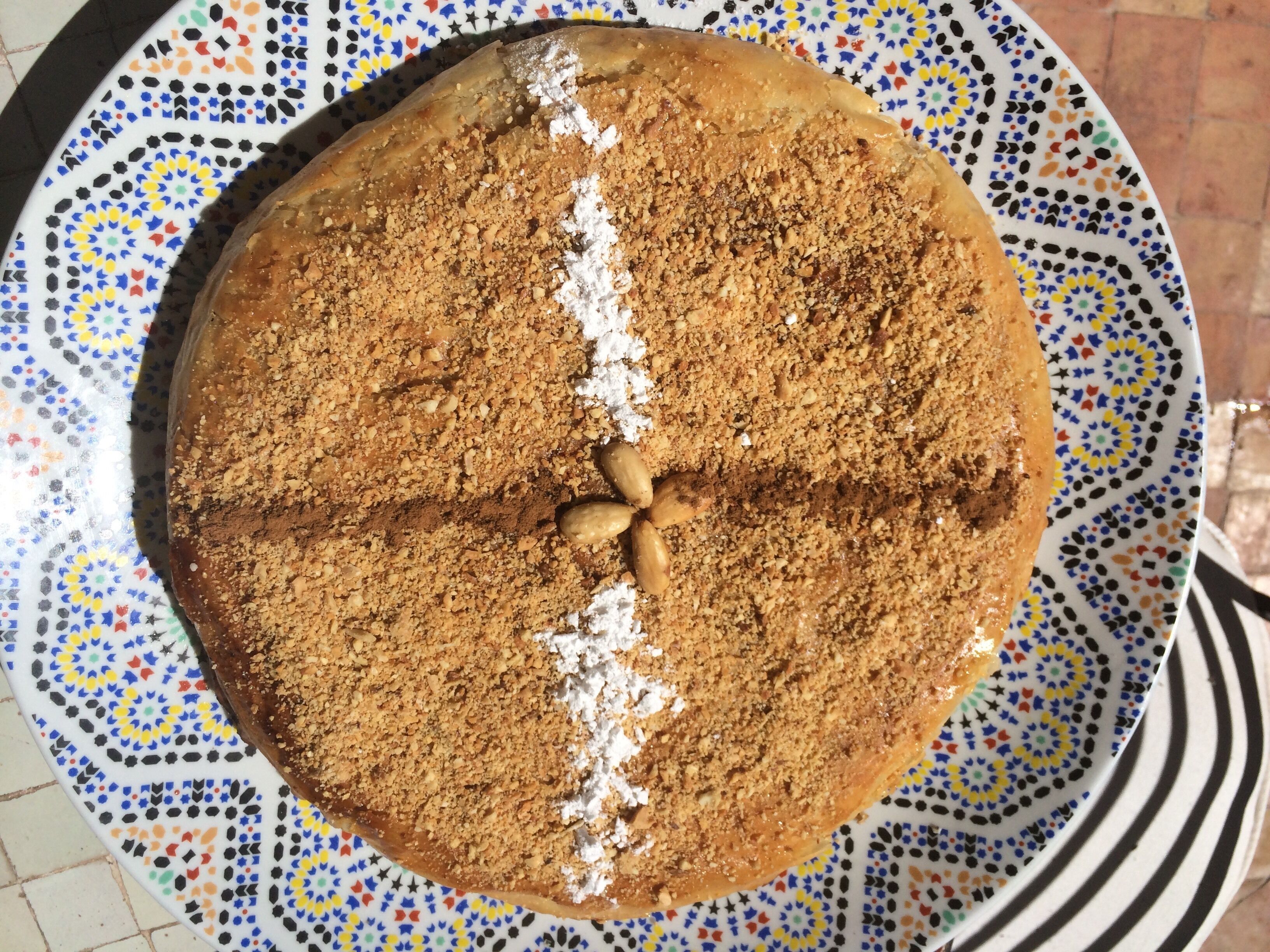 A round cake with a crumbly topping and almonds on a patterned plate.