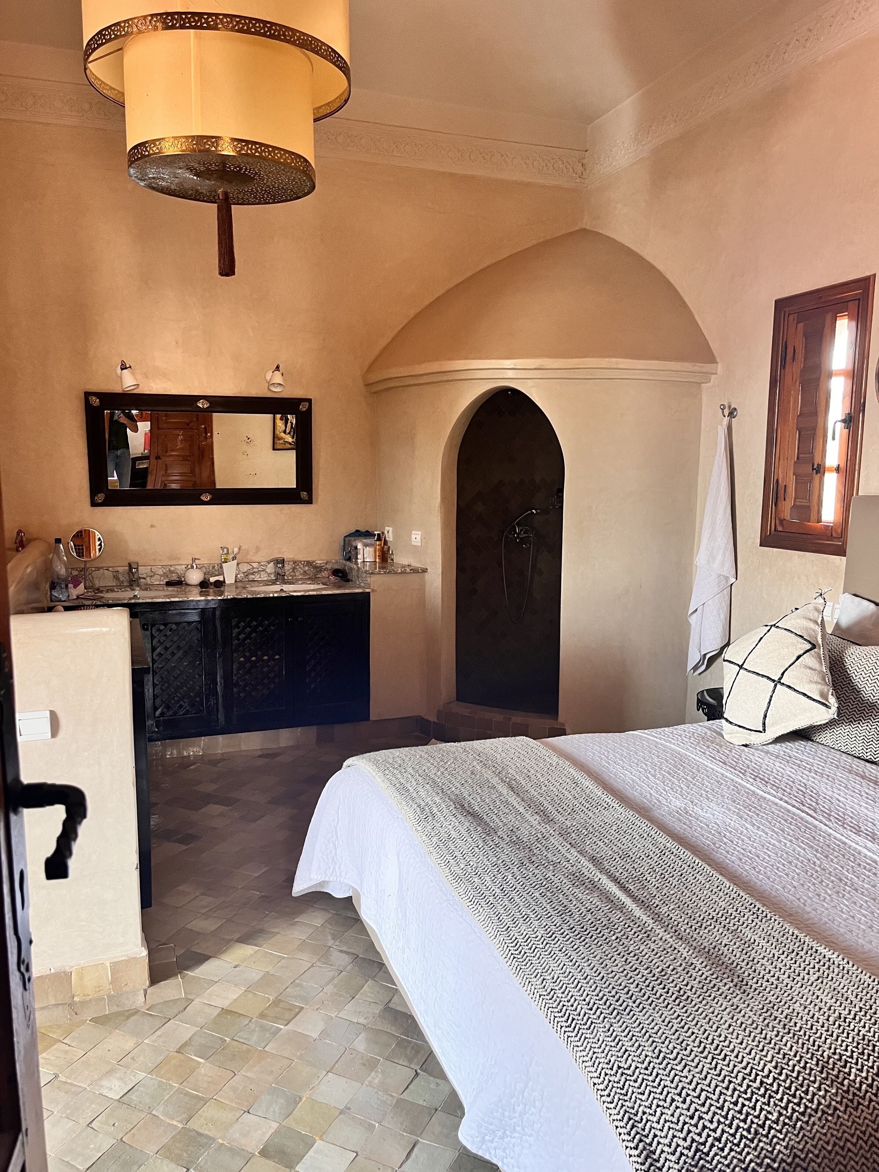 Un dormitorio con cama, mesita de noche, espejo, cómoda y baño con ducha.
