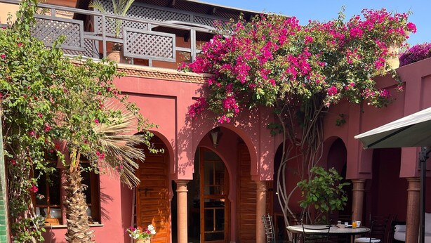 A pool area with a clear blue pool, a table with chairs, and a building with arches and a balcony. -  riad with pool - Residence Ayda - Marrakech Palmeraie. near golf (MARRAKECH)