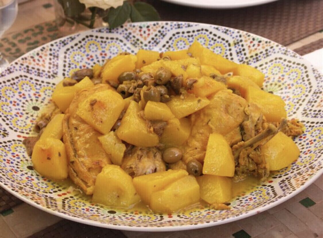 A plate of food with chunks of meat and potatoes, served on a decorative plate.