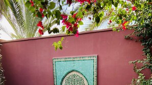 A round table set for a meal with a decorative wall and a pool in the background. -  riad with pool - Residence Ayda - Marrakech Palmeraie. near golf (MARRAKECH)