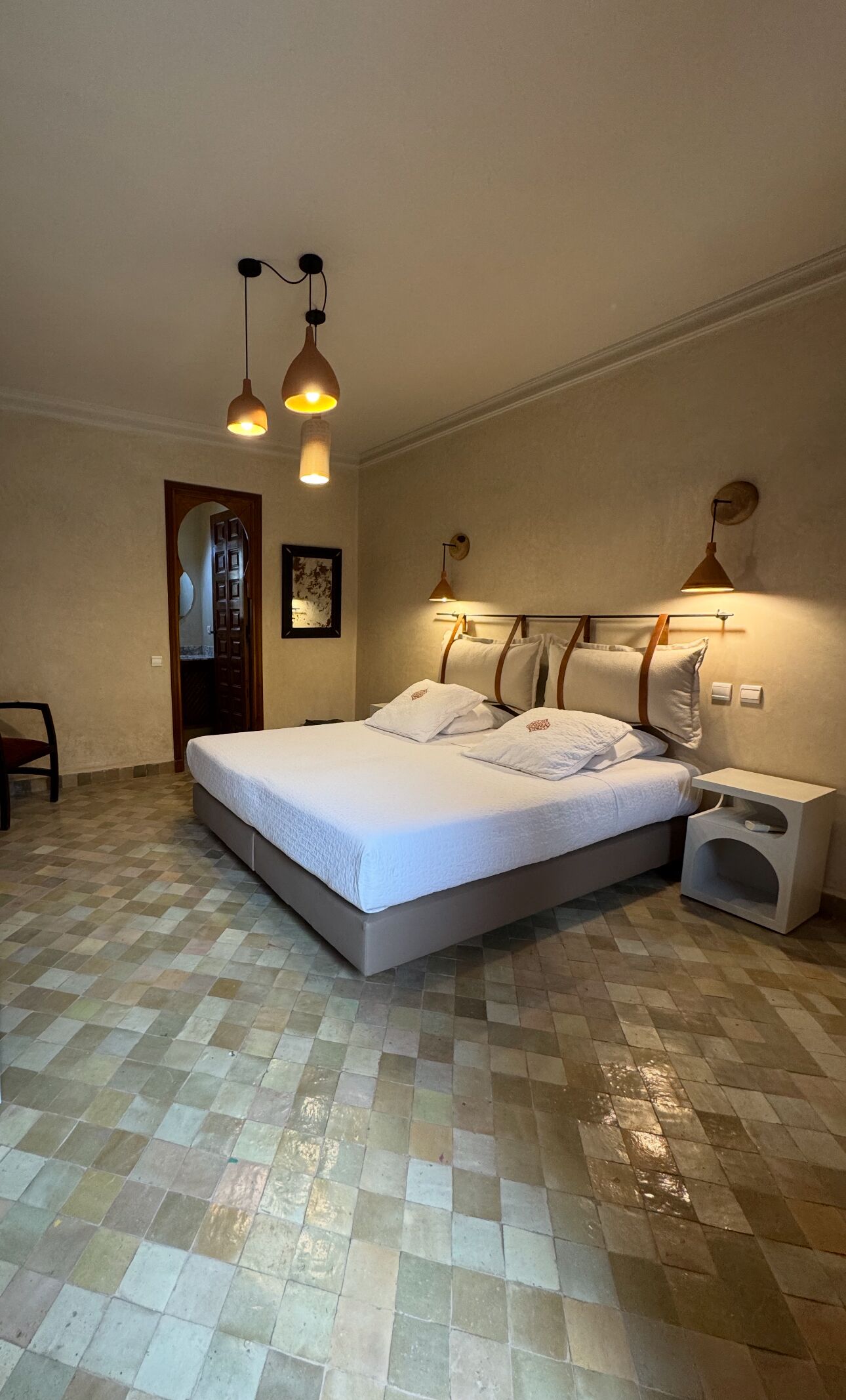 A bedroom with a large bed, two bedside lamps, a nightstand, and a mirror.