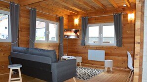 Ein Holzblockbau-Innenraum mit einer Couch, zwei kleinen Tischen, einem Fernseher und einem Sessel.
