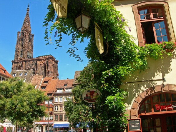 Un bâtiment historique doté d’une haute flèche, entouré d’arbres et d’autres bâtiments à l’architecture traditionnelle.