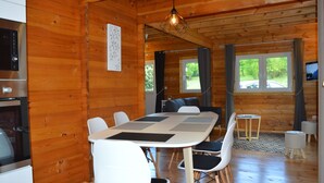 Ein Holzblockhaus-Innenraum mit Esstisch, Stühlen, einer Küchenzeile und einem Fernseher.
