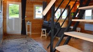 Ein Holzblockhaus-Interieur mit Treppe, einer Couch, einem kleinen Hocker und einem gemusterten Teppich.