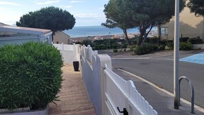 A narrow pathway with a white fence, a potted plant, and a view of the sea and buildings in the distance. - Villa, all mod cons, enclosed with seaside view (Fleury)