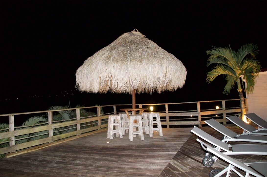 A wooden deck with a thatched umbrella, lounge chairs, and a table with chairs.