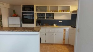 A compact kitchen with white cabinets, a microwave, a stove, and a small refrigerator.
