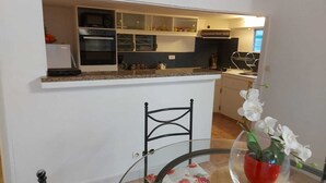A compact kitchen with a built-in oven, microwave, and a small dining area with a chair and table.
